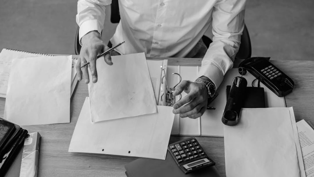 A business professional organizing documents at a busy office desk, emphasizing productivity (Nigel Farage), context for UK