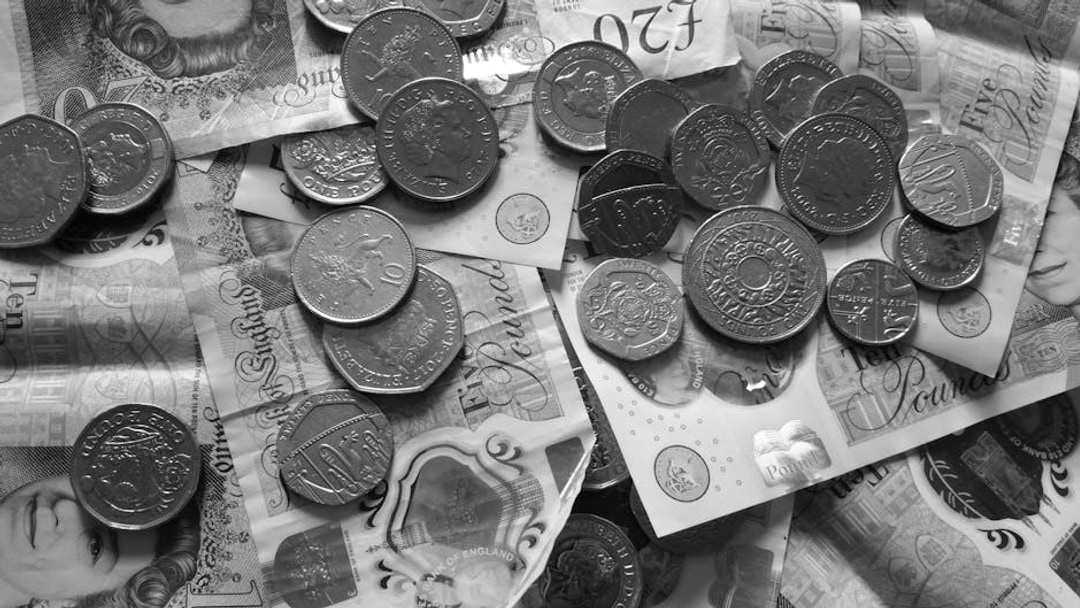 Close-up of various British pound coins and banknotes displaying Queen Elizabeth II's portrait, illustrating FTSE 100