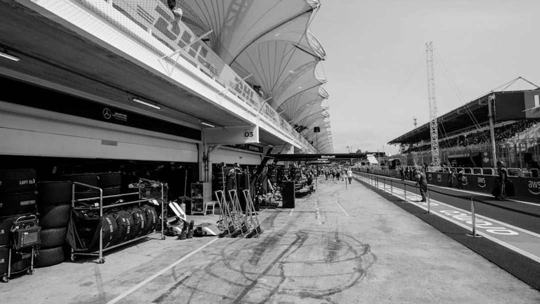 View of a Formula 1 pit lane with garage preparations and racing equipment, illustrating Mercedes Alpine F1 bid