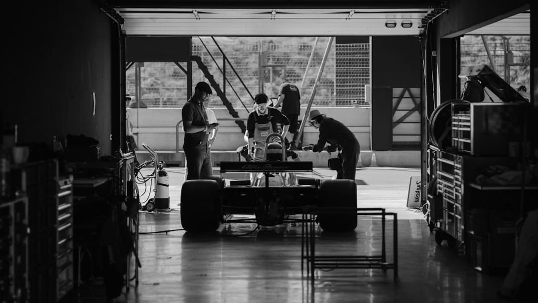 a group of people standing around a car in a garage, illustrating Sky Sports F1 deal