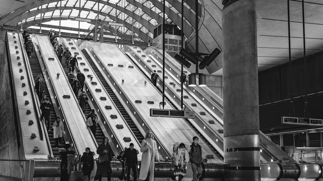 People commuting on escalators inside Canary Wharf Station, London, illustrating UK PMI job cuts